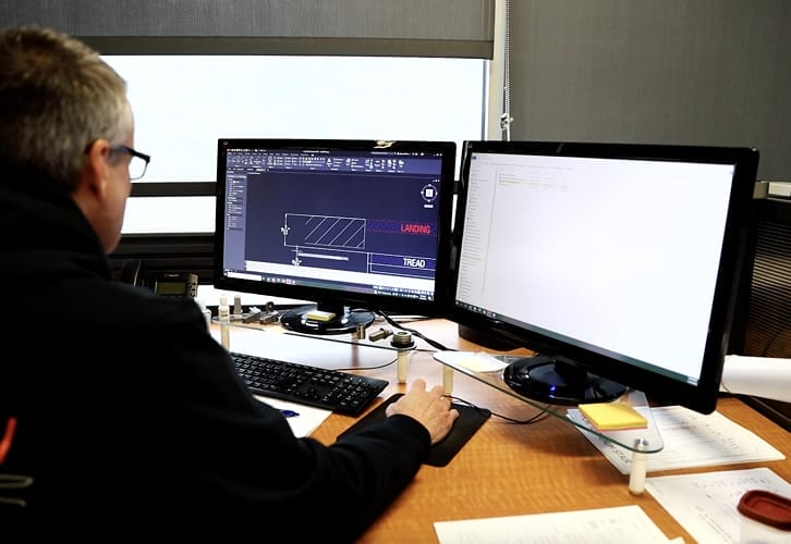 Engineer reviewing a spiral staircase CAD drawing with tread and landing dimensions on dual monitors