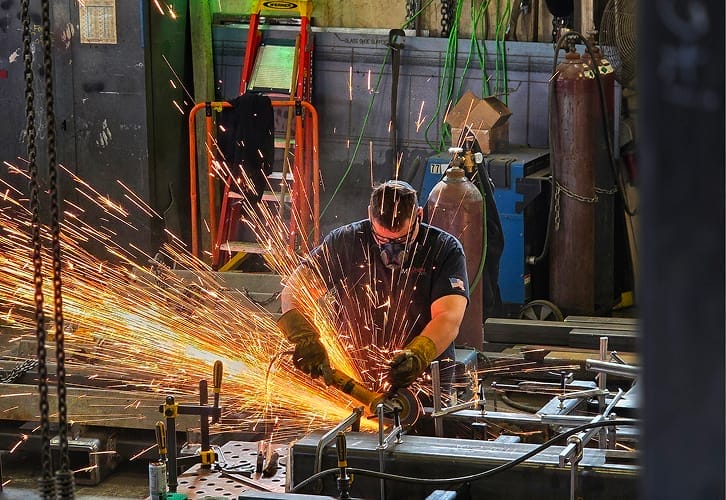 Technician welding and grinding steel staircase components, sparks visible in the fabrication shop