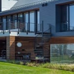 Black Builder Standard Spiral staircase connecting a deck to a patio outside a modern home with metal roofing and wood-slat siding