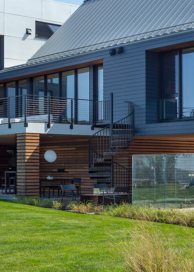 Black Builder Standard Spiral staircase connecting a deck to a patio outside a modern home with metal roofing and wood-slat siding