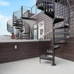 Row of black Builder Standard Spiral series staircases on a rooftop deck of a multi-unit building with dark siding