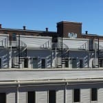 Rooftop view of black Builder Standard Spiral series staircases spaced along a row of rooftop decks on a multi-unit residential building