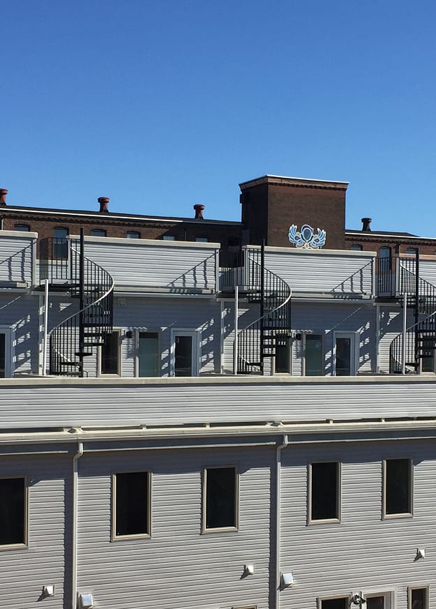 Rooftop view of black Builder Standard Spiral series staircases spaced along a row of rooftop decks on a multi-unit residential building