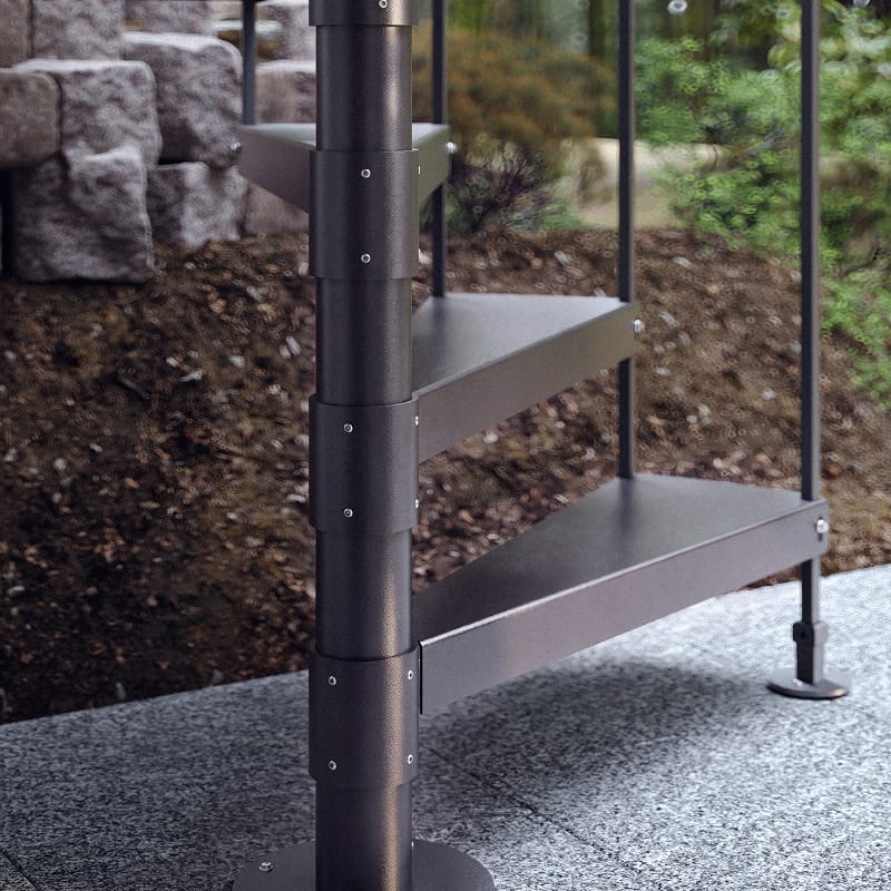Close-up of a Half Turn spiral staircase center pole showing stacked metal treads and spindle railing against a stone retaining wall.