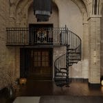 Victorian spiral staircase in a grand entryway with arched brick walls and a chandelier