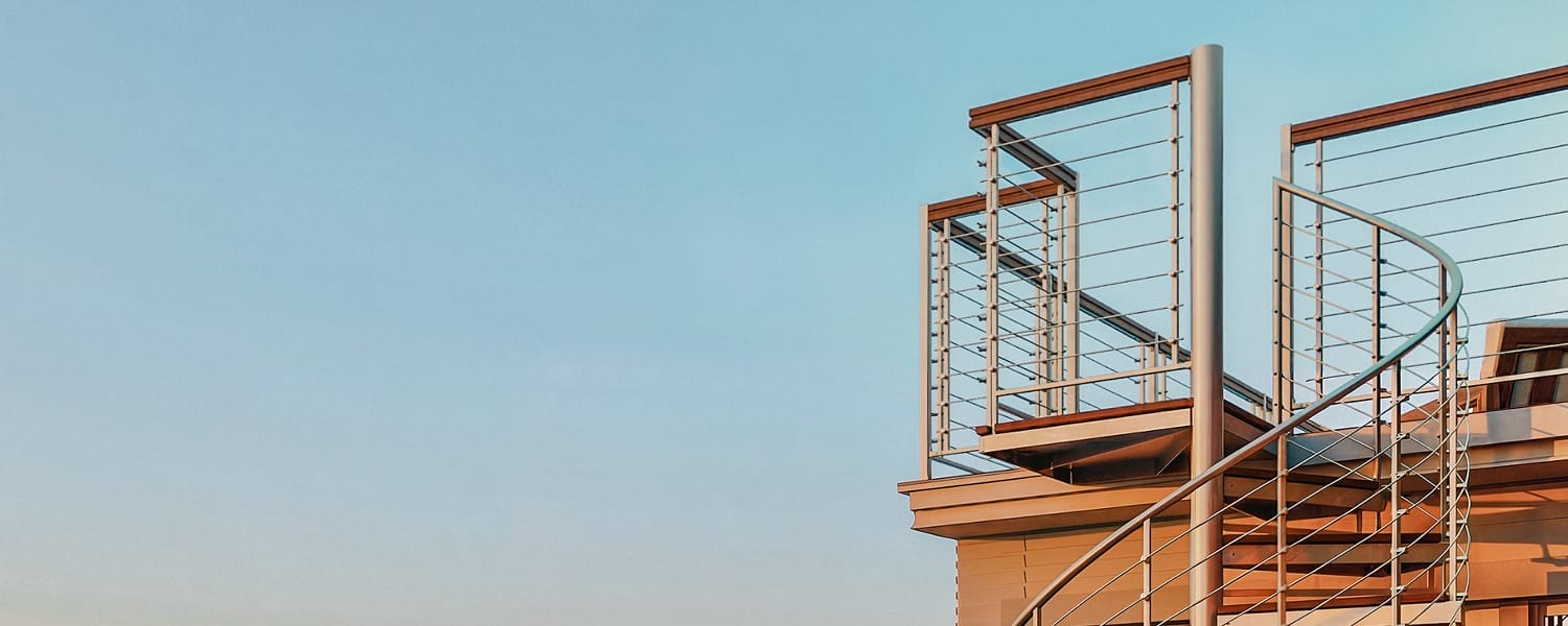Outdoor spiral staircase with mulit-line rail system leading to a rooftop deck against a clear sky