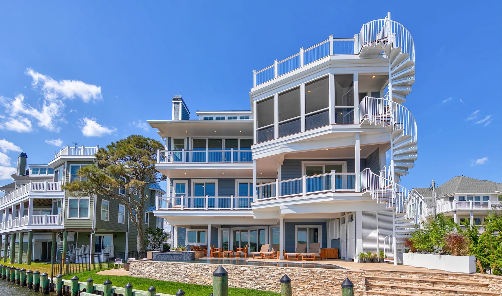 White exterior spiral staircase connecting multiple deck levels on a waterfront home, with a pool and dock below
