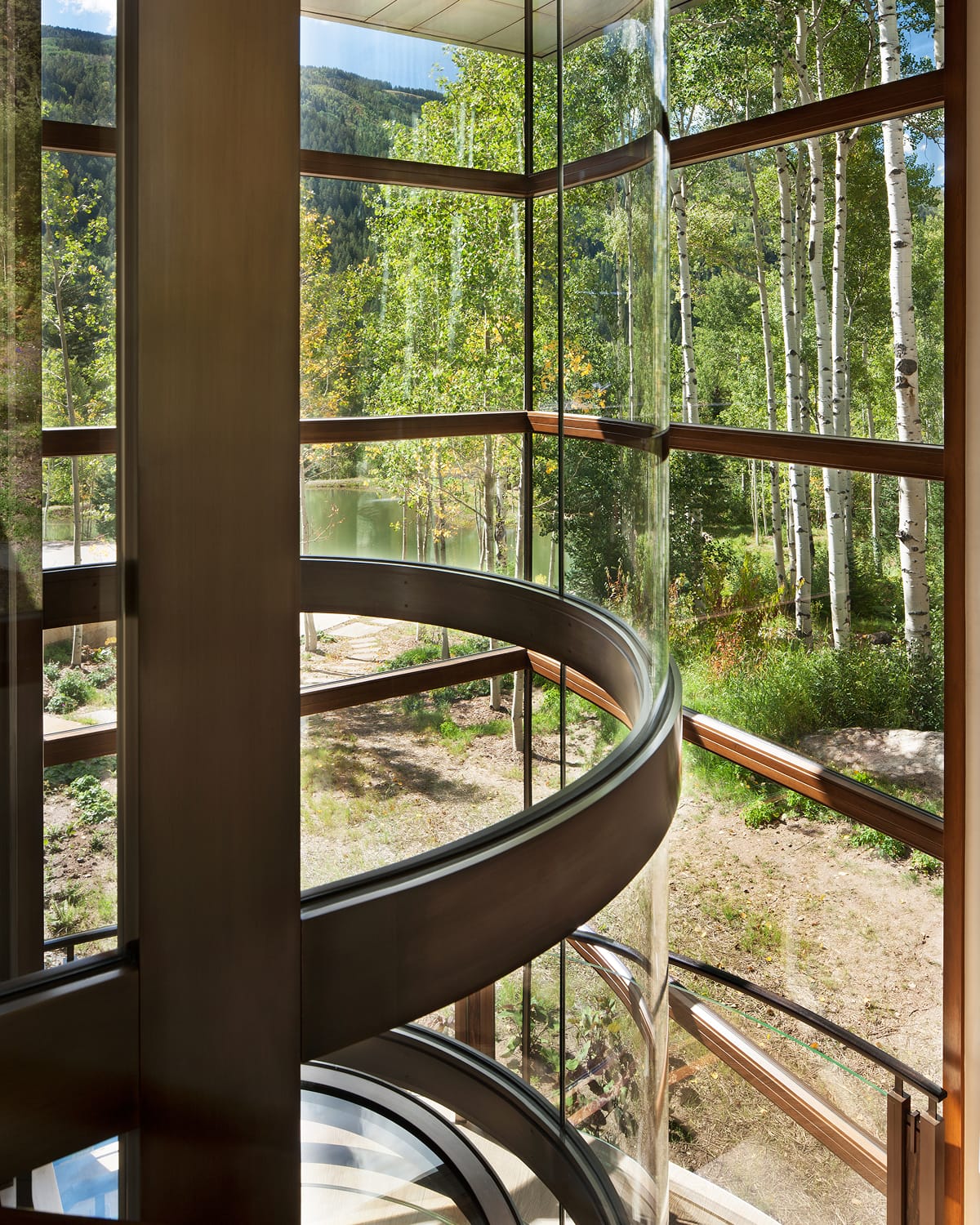 Close view from beside a curved glass elevator shaft, looking out through floor-to-ceiling glass panels