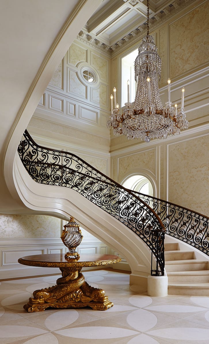 Custom sweeping curved staircase with ornate scroll-pattern railing in a grand entry hall