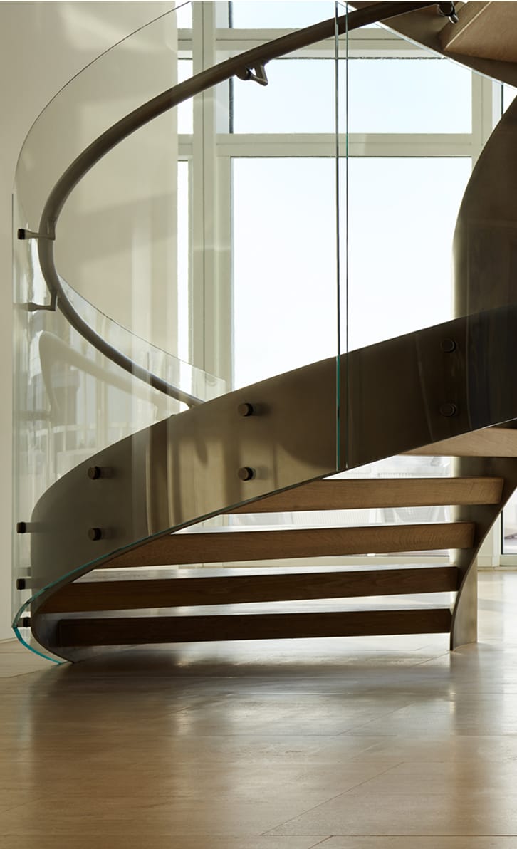 Custom curved floating staircase with glass railing and wood treads cantilevered from a metal stringer, set against floor-to-ceiling windows