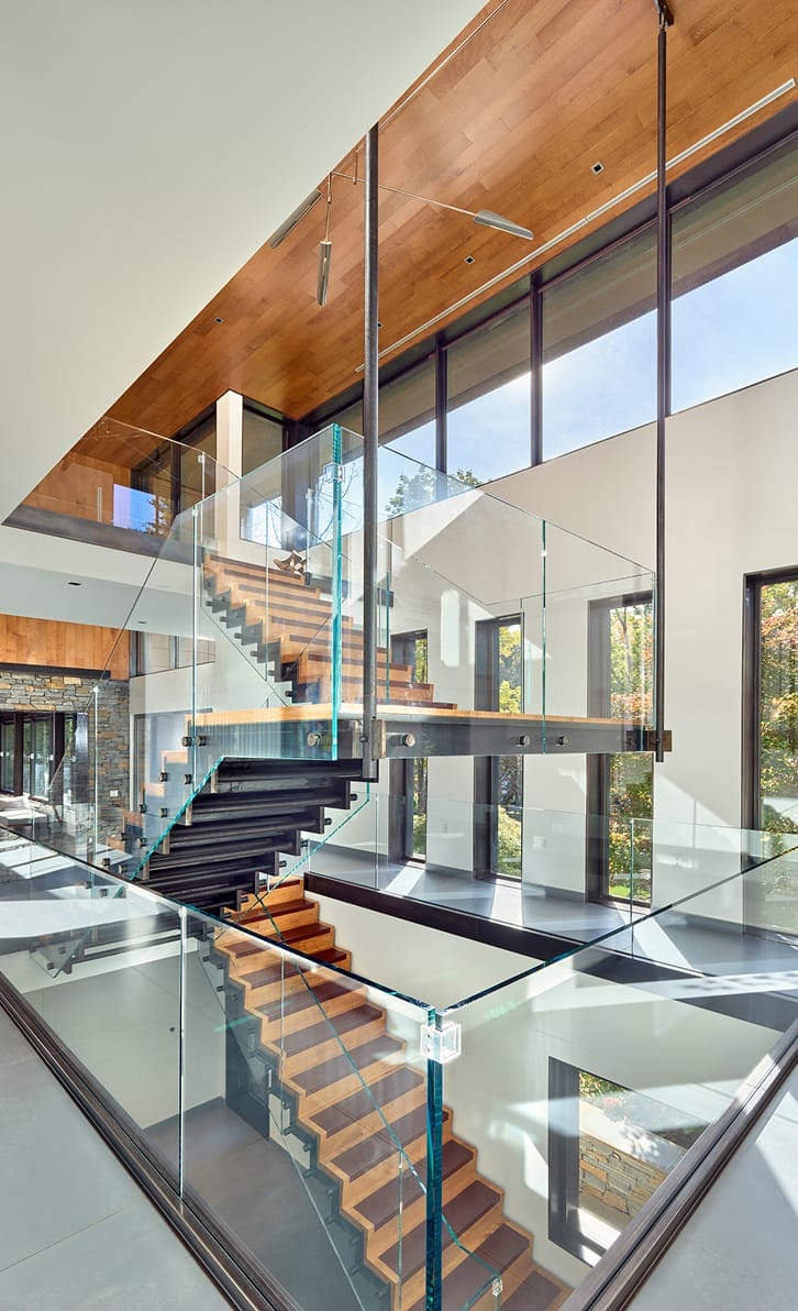 Custom floating staircase with wood and a glass railing, spanning multiple floors beneath a wood ceiling and glass walls