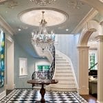 Close view of a curved staircase's scrolled iron railing and marble treads, framed against pale blue walls and a black-and-white diamond marble floor