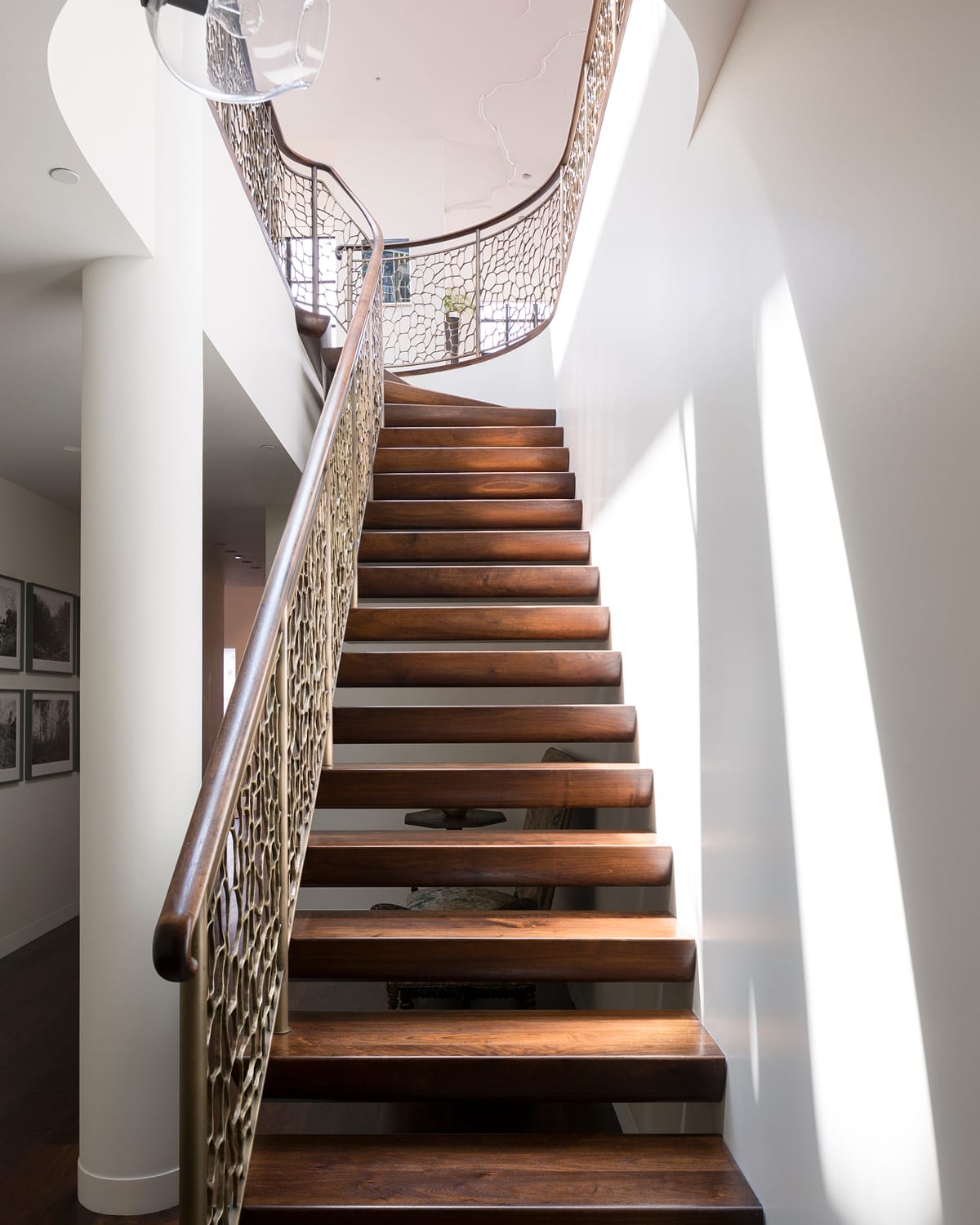 Floating staircase with dark wood treads and a metal railing cast in an organic, cell-like lattice pattern, curving up two stories beside a sunlit white stairwell