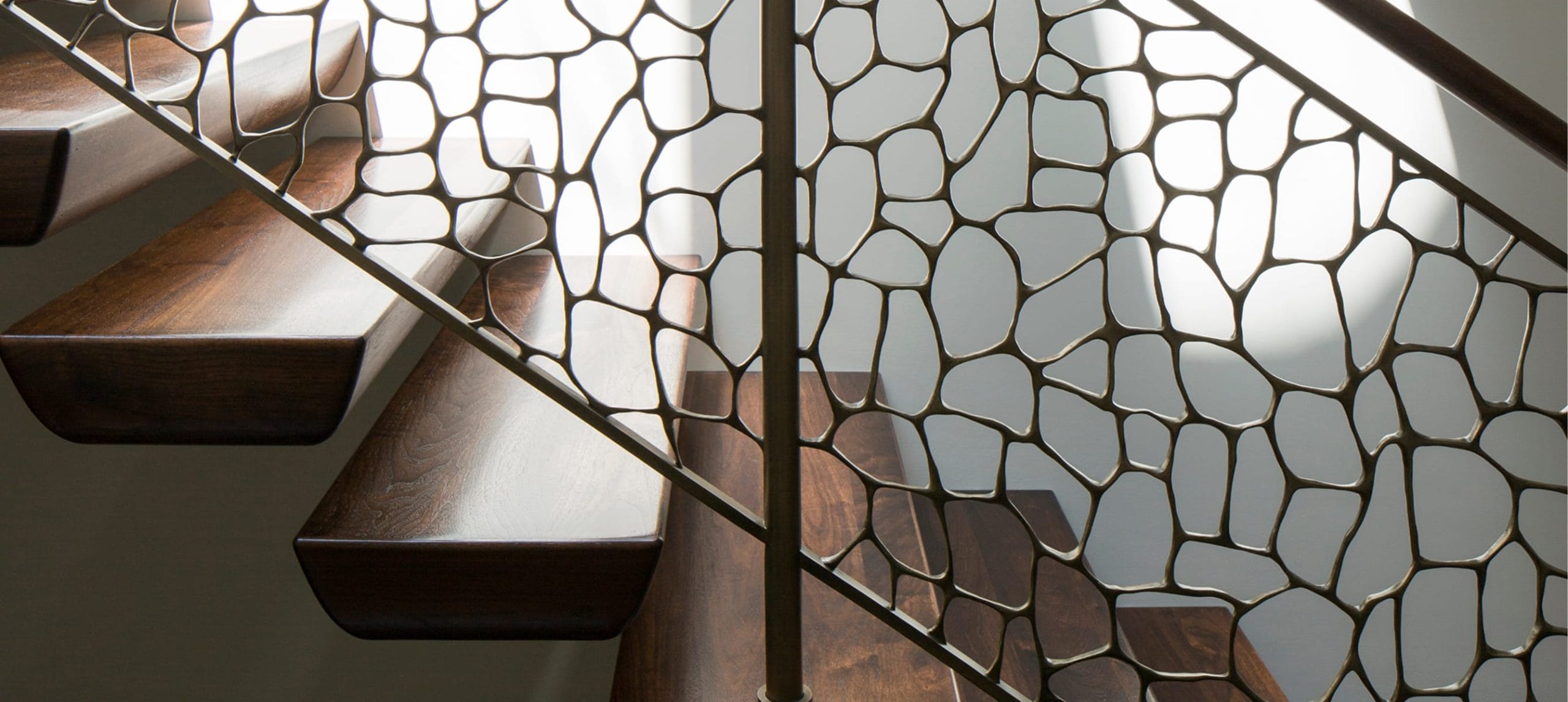 Close-up of an organic perforated bronze railing panel beside dark wood floating treads