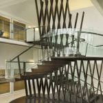 Close view of a sculptural crisscrossed metal installation enclosing a dark wood floating staircase with glass railings