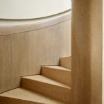 Close detail of light wood stair treads meeting a curved wood-paneled wall and round newel post