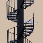 Rendering of a black steel spiral staircase with straight spindle railings and perforated metal treads, wrapping a central support pole with a square landing platform, on a plain tan background