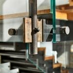 Close detail of a steel bracket and bolt connection joining a glass railing panel to a floating staircase's steel support