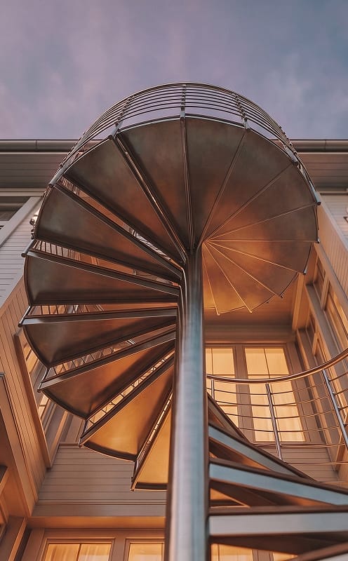 Low-angle view looking up through the underside of a metal spiral staircase against a dusk sky