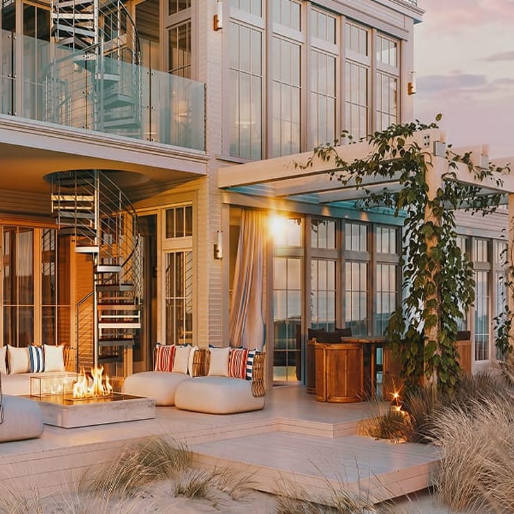 Coastal home exterior with a metal spiral staircase on the balcony, outdoor lounge seating, and a fire pit at sunset