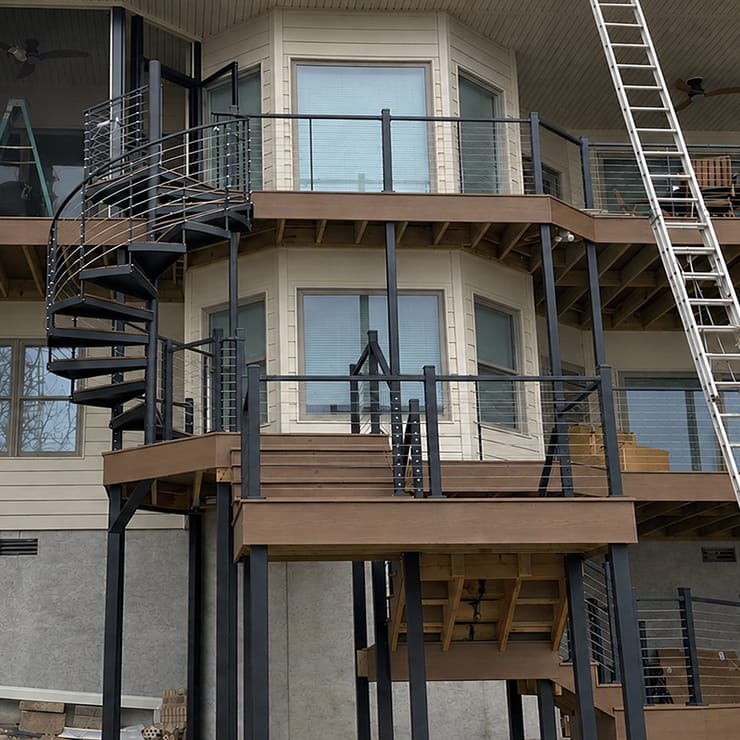 Outdoor spiral staircase connecting multi-level decks on a home under construction, with ladders and exposed framing