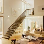 Standard Floating staircase with open-riser wood treads and a black spindle railing in a bright living room with a glass-railed loft above